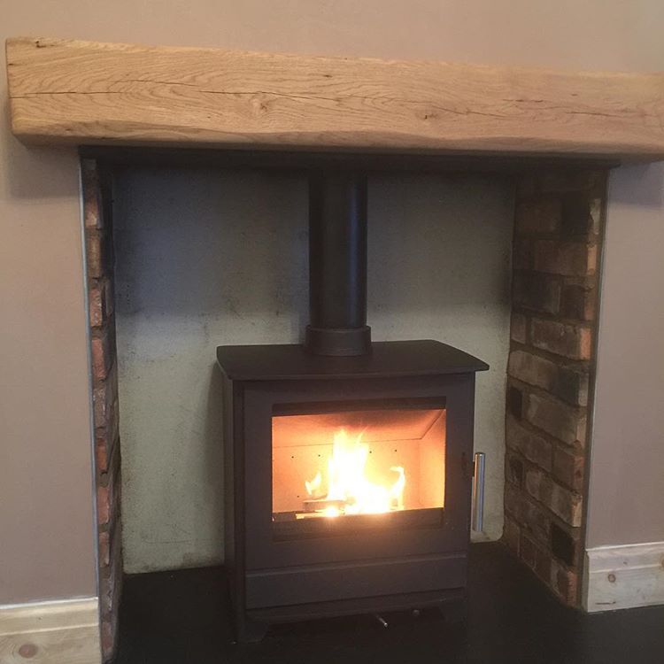 A lit wood burning stove under an oak beam, installed by Cottage Stoves Wirral